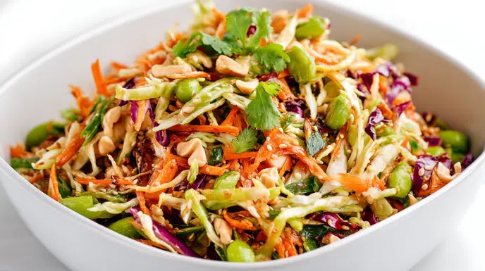 asian crunch salad recipe with shredded green and purple cabbage carrots edamame snap peas wonton strips cashews and sesame seeds in sesame ginger dressing