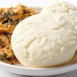 fufu recipe smooth round balls of west african cassava and plantain fufu in white bowl beside dark bowl of egusi soup with palm oil