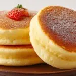 Japanese pancakes tall and fluffy with powdered sugar and syrup served on a plate