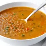 Warm Lebanese lentil soup served in a bowl with lemon slices, fresh herbs, and soft flatbread on the side.