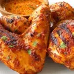 Spicy peri peri chicken served with crispy roasted potatoes and fresh herbs on a rustic plate.
