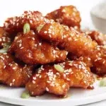 Sticky sesame chicken coated in glossy sesame sauce and topped with sesame seeds and green onions