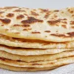 turkish bread recipe soft fluffy bazlama flatbread cooked on skillet showing golden brown spots and dramatic puff with melted butter and dipping bowl alongside