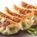 Japanese gyoza dumplings pan-fried until golden and crispy, served with a savory dipping sauce.