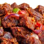 Nigerian Asun made with spicy grilled goat meat, peppers, onions, and bold seasonings, served on a platter.