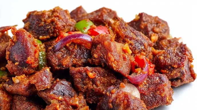 Nigerian Asun made with spicy grilled goat meat, peppers, onions, and bold seasonings, served on a platter.