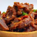 Nkwobi spicy cow foot served with tender cow foot pieces coated in a rich spicy palm oil sauce and garnished with onions.