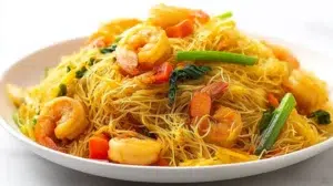 Singapore noodles stir-fried with rice noodles, vegetables, shrimp, and curry spices in a colorful wok dish.
