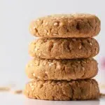 Golden tahini cookies with a soft crumbly texture, arranged on a plate and sprinkled with sesame seeds.