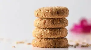 Golden tahini cookies with a soft crumbly texture, arranged on a plate and sprinkled with sesame seeds.