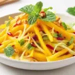 Thai mango salad made with fresh mango, colorful vegetables, herbs, and a tangy dressing, served in a bowl.