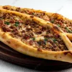 Turkish pide flatbread topped with seasoned minced lamb, vegetables, and herbs, baked until golden and crisp.