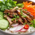 Vietnamese Banh Mi bowl served with seasoned meat, rice, pickled vegetables, cucumber, fresh herbs, and a flavorful sauce.