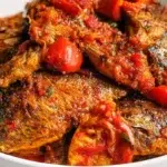 Peppered croaker fish served with crispy fried croaker coated in a spicy pepper sauce and garnished with sliced onions and fresh herbs.
