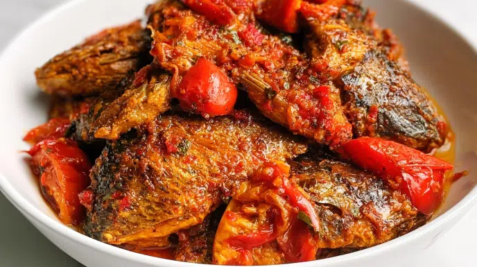 Peppered croaker fish served with crispy fried croaker coated in a spicy pepper sauce and garnished with sliced onions and fresh herbs.